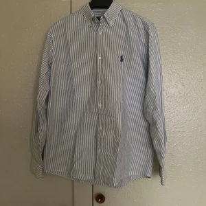Randig skjorta från Polo Ralph Lauren - Snygg randig skjorta från Polo Ralph Lauren i blått och vitt. Skjortan har en broderad logga på bröstet och är i slim fit. Perfekt för en stilren look.