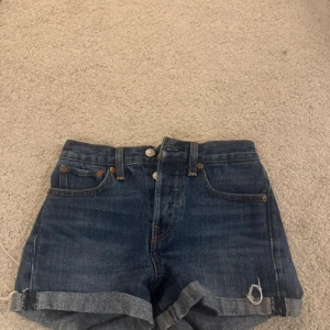 Blå jeansshorts från Levi's - Säljer ett par klassiska blå jeansshorts från Levi's med upprullade benslut och knappgylf. Shortsen har fem fickor och en läderpatch med logga på baksidan. Perfekta för en avslappnad stil.