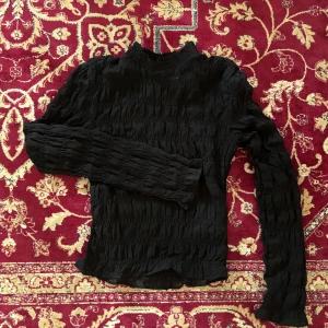 Svart ribbad tröja - Säljer en svart ribbad tröja med långärmad design. Tröjan har en unik textur och är perfekt för att ge en stilren look. Luftig och genomskinlig material. Passar bra till både jeans och kjol.