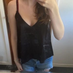 Svart linnetopp från Lager 157 - Säljer en svart linnetopp från Lager 157 i storlek S. Toppen har tunna axelband och v-ringning framtill. Materialet är glansigt och känns lyxigt, perfekt för att lyfta vilken outfit som helst.
