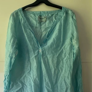 Ljusblå blus från Copenhagen Luxe XS - Supersöt ljusblå blus från Copenhagen Luxe i tunn bomull. V-ringad med knappar och glittriga pärldetaljer framtill. Långärmad och perfekt för vår och sommar. Sval och luftig, passar till jeans eller shorts. Använd en gång, bröst 100cm.