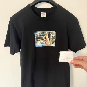 Supreme svart t-shirt med tryck - Svart t-shirt från Supreme i 100% bomull med ett stort grafiskt tryck framtill som har blå ram och Supreme-logga. Klassisk passform med rund hals och korta ärmar. Perfekt för dig som gillar streetwear och vill sticka ut. Har använt bara 3 gånger.  