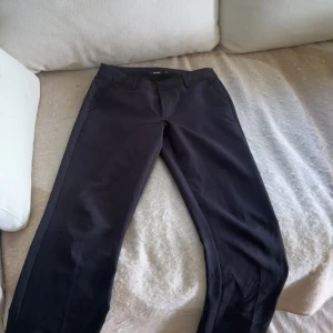 Svarta kostymbyxor från Bikbok - Snygga svarta kostymbyxor från Bikbok med klassisk rak passform. Byxorna har hällor för bälte, sidfickor fram och två fuskfickor bak. Perfekta för en clean och stilren look. Materialet känns mjukt och följsamt.