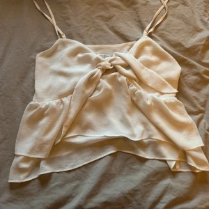 Ljus linnetopp med knyt fram - Supersöt ljus linnetopp från Zalando med smala axelband och snygg knytning framtill. Toppen har en lätt volangig nederkant och är tillverkad i ett tunt, luftigt material som passar perfekt till varma dagar. Storlek M