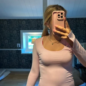 Ljusrosa långärmad topp - Supersöt ljusrosa långärmad topp med rundad urringning och figurnära passform. Ärmarna har en liten volangdetalj vid mudden som ger en extra touch. Perfekt att styla med jeans eller kjol för en fräsch look.