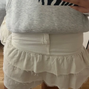 Vit volangkjol i jeans med råa kanter - Supersöt vit kort jeanskjol med volanger och råa kanter. Kjolen har klassisk jeansmidja med knapp och fickor framtill. Perfekt för dig som gillar en trendig och lekfull stil med extra edge tack vare de fransiga detaljerna. Säljer då den inte används skriv om du undrar något💞