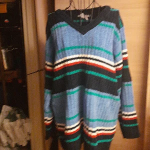 Randig stickad tröja H&M blå/grön - Säljer en oversized stickad tröja från H&M med breda ränder i blått, svart, grönt, vitt och rött. Tröjan har v-ringning och långa ärmar, perfekt för dig som gillar färg och vill ha en chill vibe. Passar dig som vill ha en mysig och trendig look.