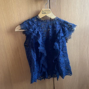 Zara spetsblues - Supersöt blå blus i spets med volangdetaljer framtill och längs ärmarna. Blusen är ärmlös och har en romantisk känsla med blommigt spetsmönster. Perfekt för dig som vill sticka ut med en feminin och trendig look.