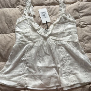 Söt vitt linne  - Superfint vit linne med volangdetaljer längs axelband och urringning. Toppen har mönster och smockad midja som ger en söt och luftig känsla. Perfekt för varma dagar och enkel att styla med jeans eller kjol. Ursprunglingspriset är 399 men jag vill bli av med den så säljer därav för 170kr. Storlek: Xs, går även att skjutera axelbanden. Säljer åt min mamma som köpt den (vill inte ha den för den är inte riktigt min stil😅)