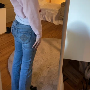 Blå bootcut jeans med broderad ficka - Säljer ett par ljusblå bootcut jeans med snyggt broderi på bakfickan. Jeansen har klassisk femficksdesign, normal passform och är tillverkade i mjukt denimtyg. Perfekta för dig som gillar en avslappnad men ändå trendig look.