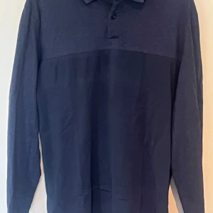 Mörkblå långärmad pikétröja Hugo Boss - Snygg mörkblå långärmad pikétröja från Hugo Boss med klassisk krage och knäppning framtill. Tröjan har en cool detalj med upphöjda ränder över bröstet och är tillverkad i mjukt bomullsmaterial. Perfekt för dig som gillar stilrena och sportiga vibes.