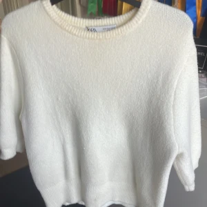 Vit stickad tröja från Zara - Supermjuk vit stickad tröja från Zara med rund halsringning och kortare ärmar. Perfekt för dig som gillar en clean och enkel stil. Tröjan har ribbade muddar och är i en skön, lite fluffig kvalitet.