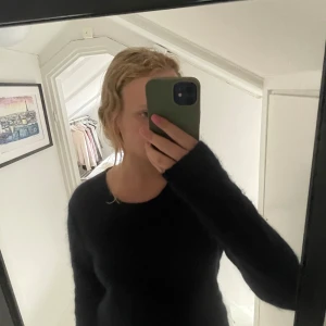 Svart fluffig tröja Second Female M - Mysig svart långärmad tröja från Second Female i storlek M. Tröjan är fluffig och har en enkel, klassisk rund halsringning. Perfekt för lager-på-lager och chill dagar. Snygg till både jeans och kjol.