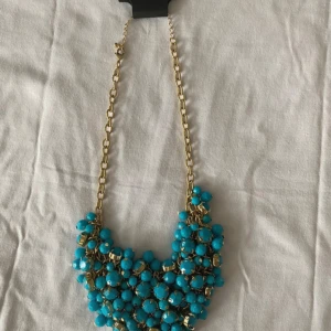 Halsband - Ett vackert och elegant halsband från Montini i guld, prytt med fina turkosa blå detaljer (inte äkta stenar). Helt nytt och oanvänt. Perfekt för att piffa upp både vardags- och festoutfits.  Passa på att bära en unik och stilfull accessoar!
