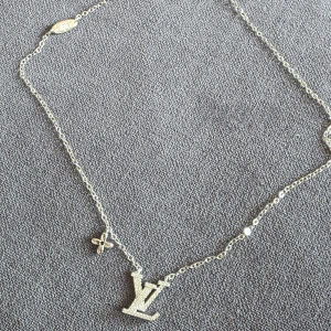 Halsband i silver - Stilrent halsband från i silverfärgad metall med glittrande logga och ikonisk blomdetalj. Kedjan är tunn och elegant, perfekt för att lyfta din look med en touch av lyx.