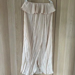 Ljusbeige offshoulder långklänning - Superfin ljusbeige långklänning med offshoulder och volang upptill. Klänningen är luftig och har en lätt, skir känsla i materialet. Perfekt för varma dagar när du vill känna dig både chill och snygg. Perfekt strandklänning!