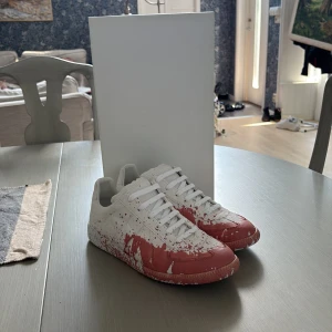 Maison margiela - Unika sneakers från Maison Margiela i vitt skinn med röda färgstänk över hela skon. SPLITTER NYA!! Aldrig använda, passar 40-41, bra pris😉