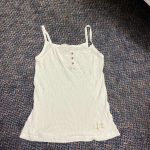 Vit ribbad linnetopp  - Supersöt vit ribbad linnetopp från Odd Molly med smala axelband, knappar framtill och liten rosett. På baksidan finns älva och nertill en tygpatch med text. 🩷.