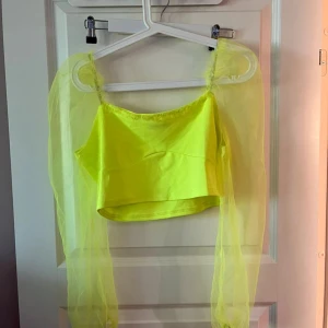 Neongul croppad topp med meshärmar - Supercool neongul croppad topp med långa transparenta meshärmar. Toppen har en rak halsringning och är perfekt för dig som vill sticka ut. Materialet är mjukt och stretchigt med tunna ärmar som ger en edgy vibe.