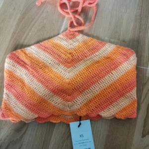 Virkad randig linnetopp XS orange - Superfin virkad linnetopp i orange, persika och beige toner. Toppen har knyt i nacken och ett snyggt zickzack-randigt mönster. Perfekt för sommarens alla äventyr och ger en riktigt chill boho-vibe.