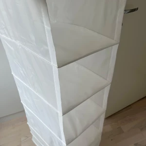 Vikbar hängförvaring i vitt och grått - Säljer fyra stycken praktiska vikbara hängförvaringar i vitt och grått. Perfekt för garderoben eller hallen, med flera hyllplan och meshdetaljer upptill. Tillverkade i lätt polyester och enkla att hänga upp på en stång eller krok. Köpt från Ikea namn Skubb. 50kr/st. 200kr/alla fyra