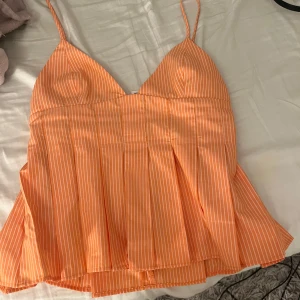 Randig orange linnetopp från Zara XS - Superfin orange linnetopp från Zara med tunna axelband och vita vertikala ränder. Toppen har v-ringning och lätt utsvängd nederdel som ger en flowy känsla. Perfekt för varma dagar och enkel att styla med jeans eller kjol.