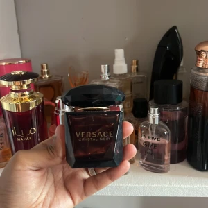 Versace Crystal Noir EdT 30ml - Versace Crystal Noir Eau de Toilette 30ml med en lyxig, mörklila glasflaska och facettslipat svart lock. Flaskan har guldiga detaljer och en elegant, mystisk vibe. Perfekt för dig som gillar exklusiva och djupa dofter.