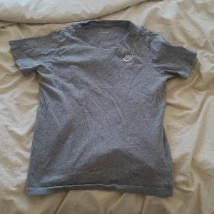 Grå Nike t-shirt - Säljer en enkel och stilren grå t-shirt från Nike med klassisk logga broderad på bröstet. T-shirten är i mjuk bomull, har rund halsringning och korta ärmar. Perfekt för en chill och sportig look.