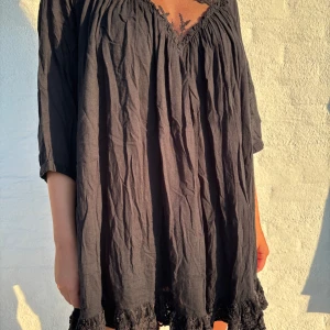 Svart kortklänning från Ajlajk med spets - Svart klänning från Ajlajk i kort modell med romantisk boho-vibe. V-ringning, spets upptill och nertill, trekvartsärmar och broderade blommor i spetsen. Volangkant nertill för extra feminin känsla 🌸 Superluftig & skön – perfekt till sommar, festival eller vardags!  📏 Storlek M 🧺 Mjuk och bekväm bomullsblandning 📬 Snabb frakt