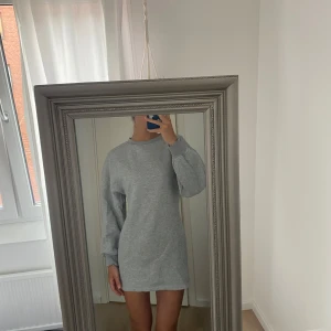 Grå oversized sweatshirtklänning - Enkel och stilren grå sweatshirtklänning med oversized passform och långa ärmar. Mjuk och skön, perfekt för chill dagar. Klassisk rund halsringning och ribbade muddar vid ärmslut. Passar dig som gillar en avslappnad vibe.