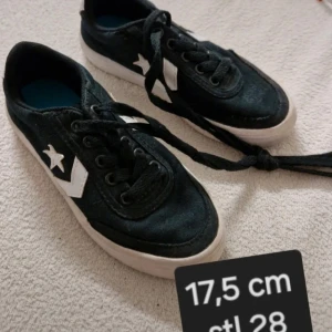 Svarta sneakers stl 28 - Snygga svarta sneakers med vita detaljer och  stjärnlogga på sidan. Skorna har svart snörning, vit sula och blå innersula. Perfekta för en cool och avslappnad stil.