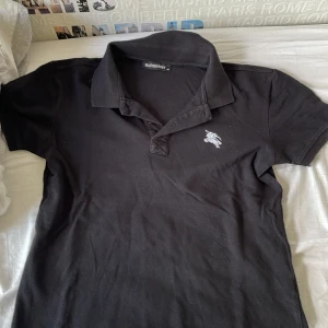 Svart piketröja med vitt tryck - Säljer en svart pikétröja med vitt tryck vid vänstra sidan av bröstet, tröjan är i bra skick och har använts mycket. Kontakta vid snabb affär.