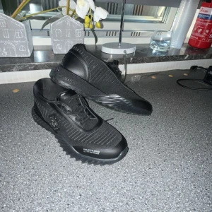 Svarta sneakers Philipp Plein strl 42 - Snygga svarta sneakers från Philipp Plein med unika hexagonmönstrade sulor och silverfärgad PP-logga på sidan. Skorna har snörning, detaljer i syntet och textil samt en cool, sportig vibe. Perfekta för dig som gillar statement-sneakers med exklusiv känsla. Och dom är knappt andvända