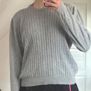 Grå kabelstickad tröja - Säljer en grå kabelstickad tröja med rund hals och långa ärmar. Tröjan har ribbade muddar.