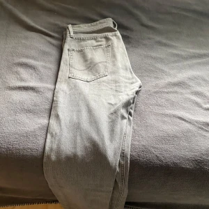 Grå jeans från Jack & Jones - Snygga grå jeans från Jack & Jones med klassisk femficksdesign och raka ben. Jeansen har en ljusgrå tvätt och subtila sömdetaljer på bakfickorna. Perfekta för dig som gillar en clean och stilren look.