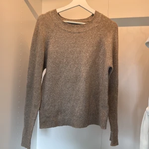 Beige stickad tröja med rund hals - En enkel och stilren beige stickad tröja med rund halsringning och långa ärmar. Tröjan har ribbade muddar vid ärmslut och nederkant, perfekt för lager-på-lager och chill vardagsstil.