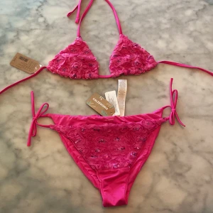 Fin calzedonia bikini med blomdetaljer - En fin calzedonia bikini oanvänd med lappar kvar. Har påsydda blomdetaljer med paljetter. Färgen är en stark rosa (inte lika lila som på bilden). Toppen har storlek 80B/75C/70D och underdelen har storlek L (känns som en M). Både toppen och underdelen är justerbara. ☀️