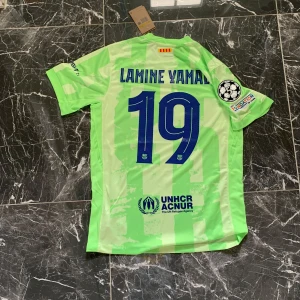 Barcelona Lamine Yamal tröja Nike S - Fräsch Barcelona fotbollströja med Lamine Yamal och nummer 19 på ryggen. Tröjan är ljusgrön med subtilt rutigt mönster, officiella tryck från Champions League och sponsorer som Spotify. Klassisk Nike-design med klubbmärke på bröstet och korta ärmar. Perfekt för fans!