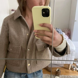Beige overshirt från Zara i ullmix - Säljer en beige overshirt från Zara i ullmix. Jackan har stora fickor framtill, guldiga tryckknappar och klassisk krage. Croppad modell med normal passform, perfekt att slänga över en hoodie eller t-shirt.