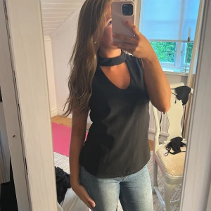 Svart ärmlös topp med choker-detalj - Snygg svart ärmlös topp med v-ringning och choker-detalj runt halsen. Tidlös och stilren modell som passar perfekt till jeans eller kjol. Toppens material känns mjukt och följsamt mot huden och ger en clean look.