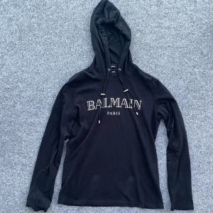 BALMAIN LOGO HOODED T-SHIRT - Äkta Balmain Paris hooded t shirt som har egenskaper av både en t-shirt och en hoodie. Asfet och i 10/10 condition. Använd bara ett fåtal gånger. Köpt på luisaviaroma hemsida. Storlek: M. Hör av er vid eventuella frågor!!