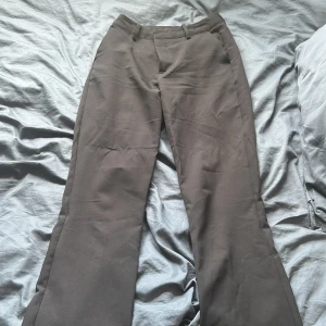 Svarta kostymbyxor från Bikbok - Klassiska svarta kostymbyxor från Bikbok i rak modell med hällor för bälte och diskreta bakfickor. Byxorna har dragkedja och knapp framtill och är tillverkade i ett mjukt tyg som känns skönt mot huden. Perfekta för en clean och stilren look.