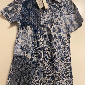 skjorta - Säljer en helt ny skjorta i marinblått och vitt mönster – en riktigt fin färgkombination! 📏 Storlek: 34/36 👘 Korta ärmar med blommigt mönster i marinblå nyans 🌬️ Lätt och luftig, perfekt för vår och sommar 🎀 Prislappen sitter kvar (utan pris) 💯 Aldrig använd  En mjuk och sval skjorta som är både stilren och bekväm – lätt att matcha! 