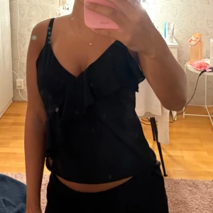 Volang linne från h&m - Superfint svart linne från h&m med en fin volang. Jätte skönt och går att fixa banden längre eller kortare för rätt passform. Storlek S!