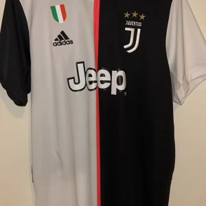Juventus De Ligt matchtröja Adidas L - Juventus officiella matchtröja från Adidas med De Ligt och nummer 4 på ryggen. Tröjan är svart och vit med röd detalj i mitten, kortärmad och tillverkad i Climalite-material som andas. Juventus-logga, tre stjärnor och Jeep-sponsor på bröstet.