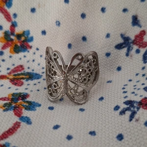 Silvrig ring med fjärilsdesign - Unik silvrig ring i form av en fjäril med detaljerat, öppet mönster. Ringen har en snygg och luftig design som verkligen sticker ut och passar perfekt för dig som gillar smycken med naturinspiration och coola detaljer.