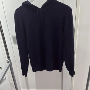 Mörkblå kashmirhoodie från Sayless - Mysig mörkblå hoodie från Sayless i lyxig kashmir. Tröjan har huva med snörning och långa ärmar, perfekt för dig som gillar en stilren och enkel look. Passar dig som vill ha något både bekvämt och snyggt till vardags. Nypris ligger på ca 900