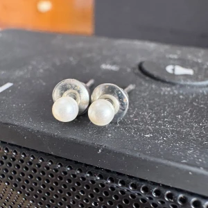 Silvriga pärlörhängen i klassisk stil - Ett par stilrena örhängen med rund vit pärla och silvrig infattning. Perfekta för dig som gillar en enkel men elegant look. Passar till allt och ger en tidlös känsla. Små och diskreta studs som är lätta att bära hela dagen.