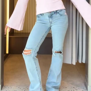 Ljusblå bootcut jeans med slitningar - Säljer ett par ljusblå bootcut jeans med låg midja och slitna detaljer vid knäna. Jeansen har klassisk femficksdesign och snygga broderade vågmönster i rosa på bakfickorna. Perfekta för en trendig och avslappnad look. Nypris: 700 kr!!! Helt nya!