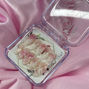 LilyDream (S);Medium Almond - Snygga gelé press-on naglar i en medium mandelform med nude bas, dekorerade med vita 3D-pärlor, vit fade och rosa rosetter, 3D handmålad nailart. Naglarna har en glansig finish och kommer i storlek S: 15 mm, 11,5 mm, 12 mm, 11 mm, 9 mm. Perfekt för dig som vill ha en söt och trendig look.